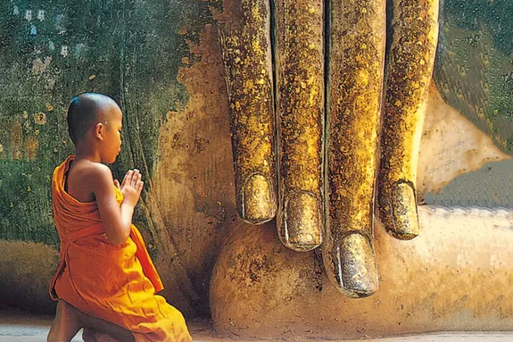 Junger Mönch vor goldener Buddha-Statue in Thailand